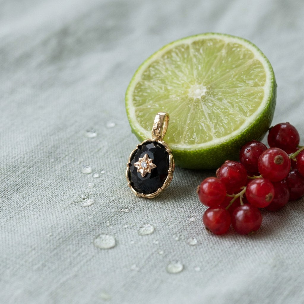 Vintage Black Onyx Starburst Charm on pale grey-green linen beside a halved lime and red currants