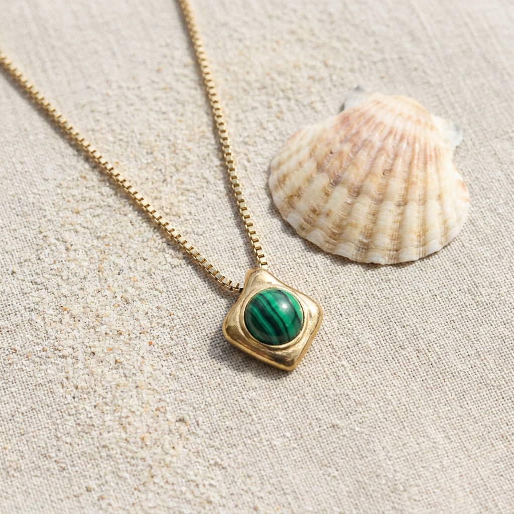 Wade Malachite Necklace on raw linen beside a scallop shell and a scatter of fine sand