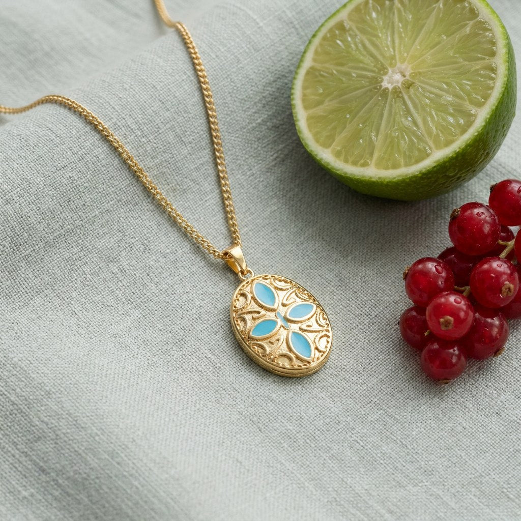 Oval Blue Petals Pendant Necklace on pale grey-green linen beside a halved lime and red currants