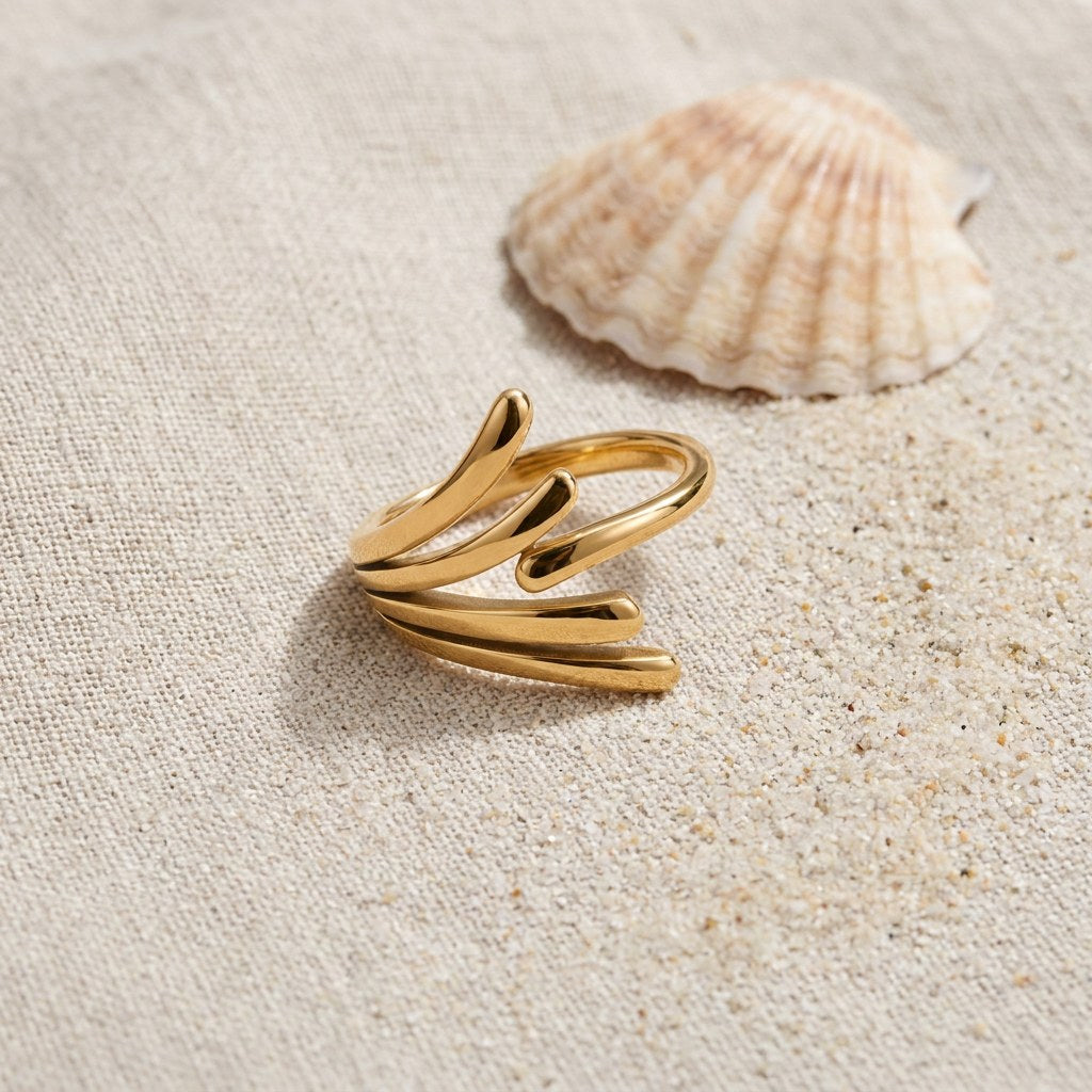 Angel Wing Ring on raw linen beside a scallop shell and a scatter of fine sand