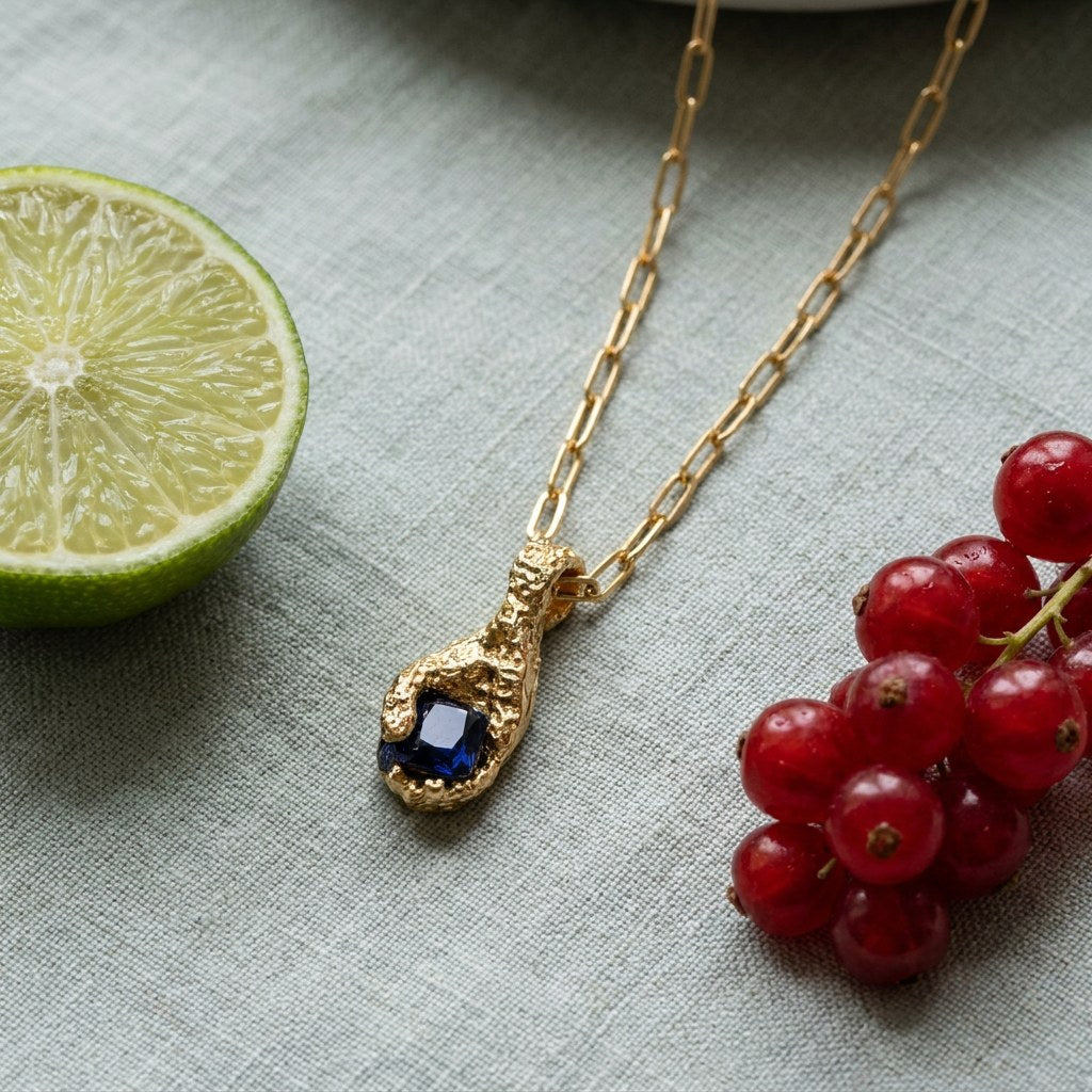 Hand of Stillness Necklace on pale grey-green linen beside a halved lime and red currants