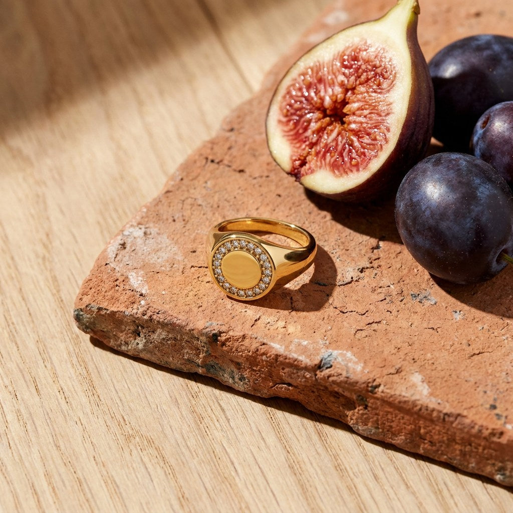 Circle Pave Signet Ring on a weathered terracotta tile with a cut fig and dark plums