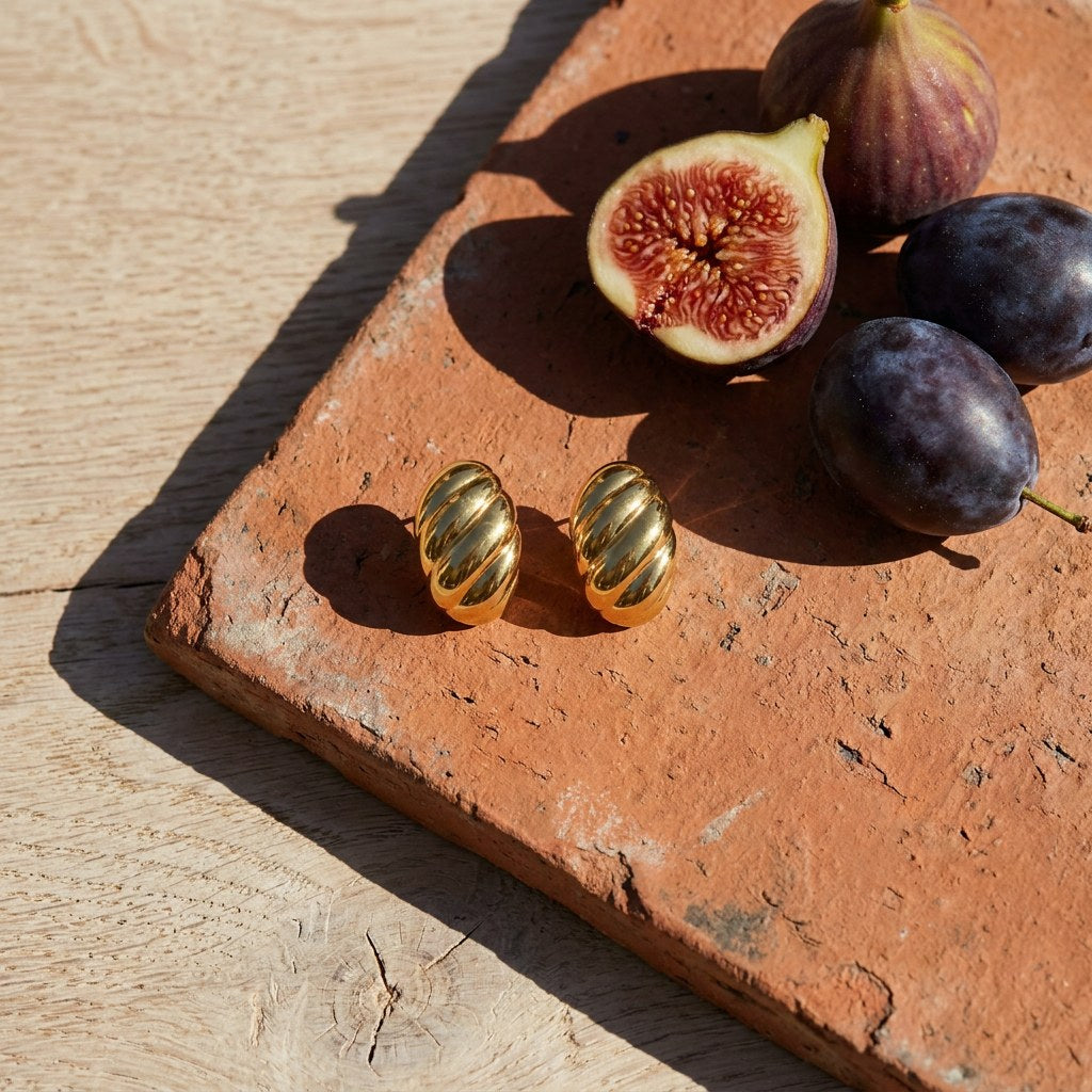 Waterproof Croissant Dome Stud Earrings on a weathered terracotta tile with a cut fig and dark plums