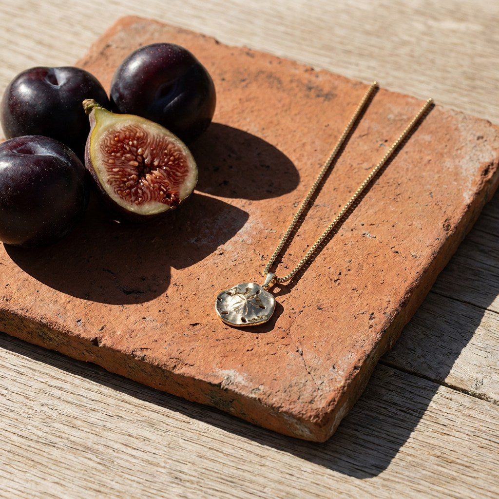 Flower Sand Dollar Necklace on a weathered terracotta tile with a cut fig and dark plums