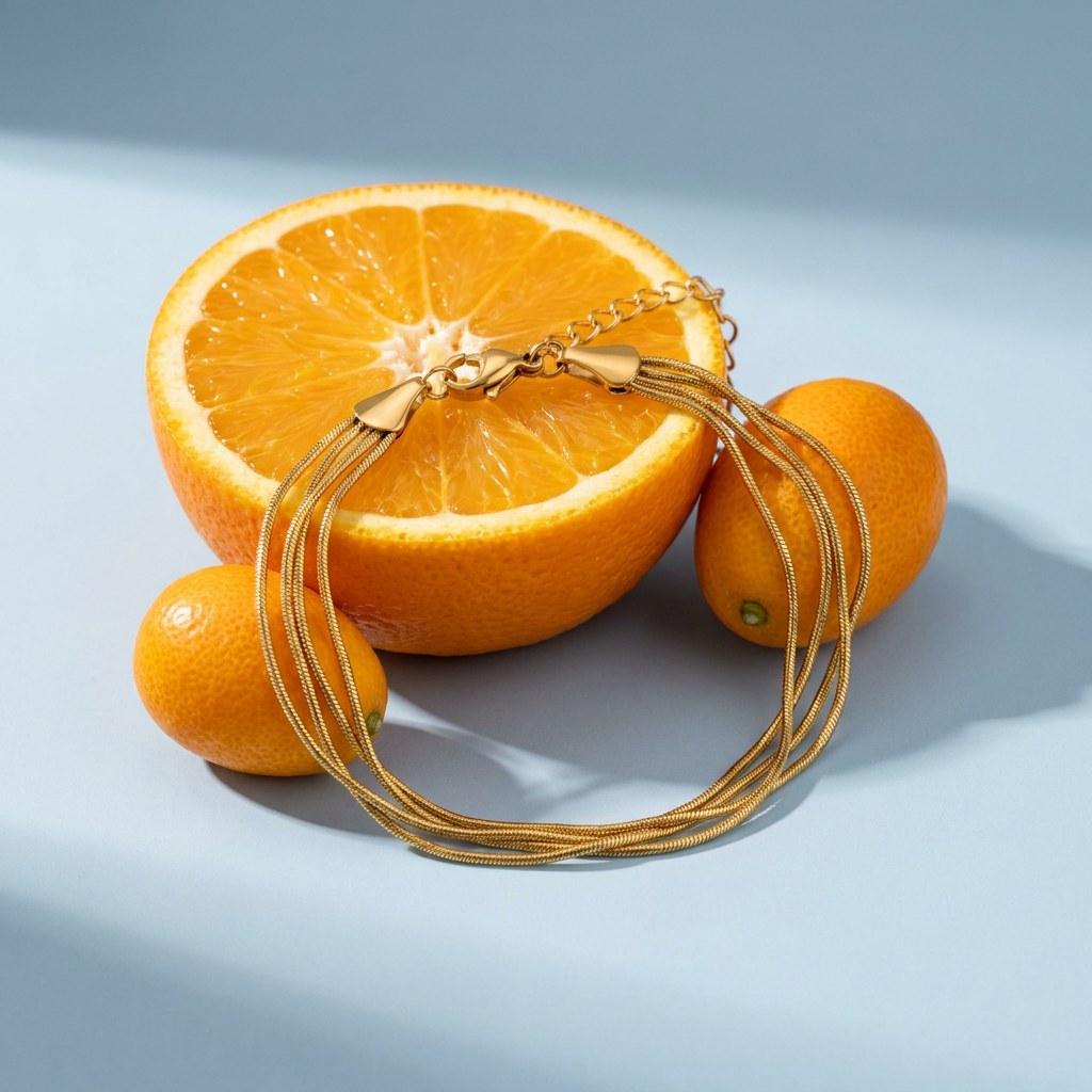 Multi Layered Snake Chain Bracelet on a pale blue backdrop beside a halved orange and two kumquats