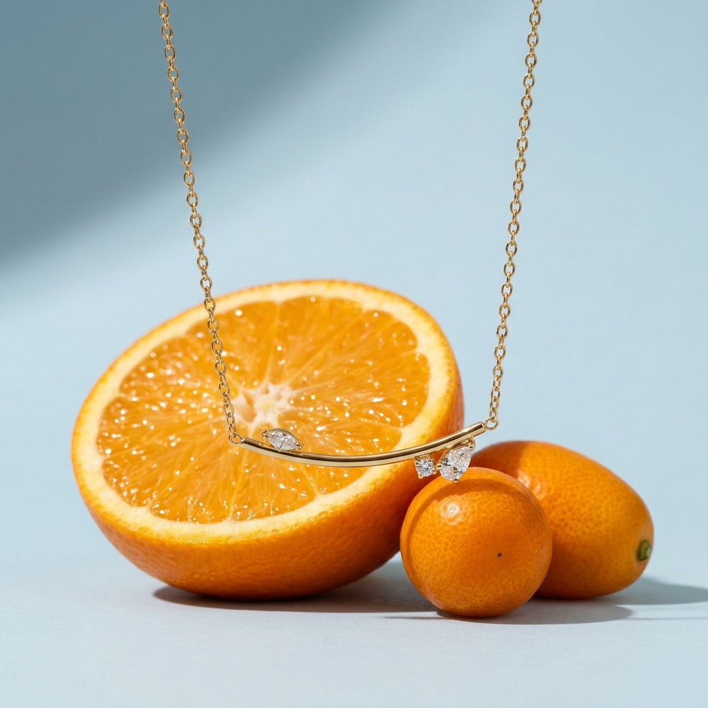 Curved Bar Necklace with CZ Leaf on a pale blue backdrop beside a halved orange and two kumquats