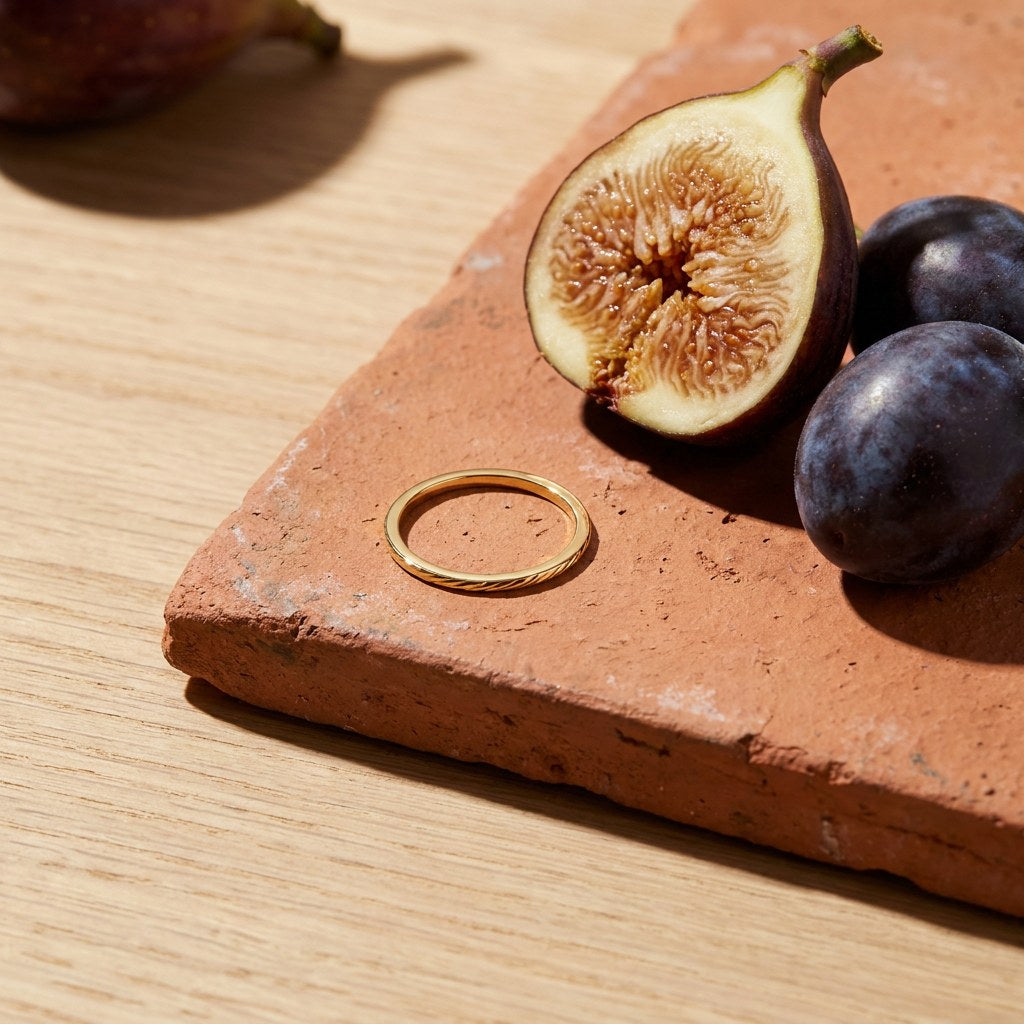 Herringbone Slim Band Ring on a weathered terracotta tile with a cut fig and dark plums