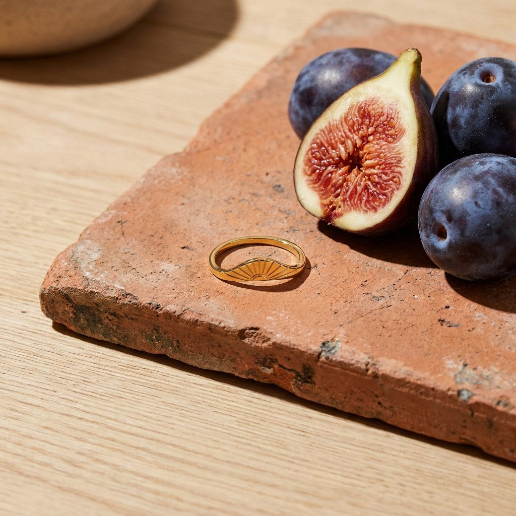 Sunrise Arc Ring on a weathered terracotta tile with a cut fig and dark plums