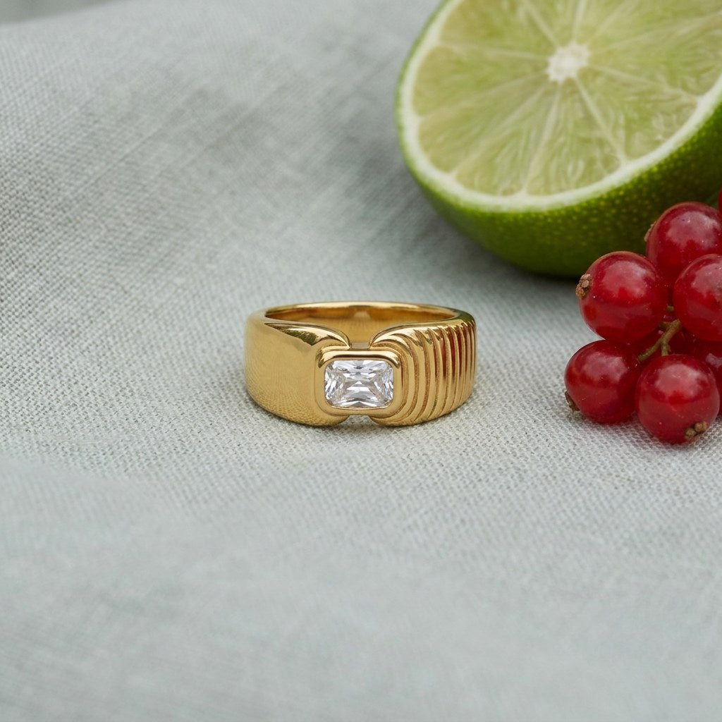 Waterproof Gold Signet Ring with Radiant Crystal on pale grey-green linen beside a halved lime and red currants