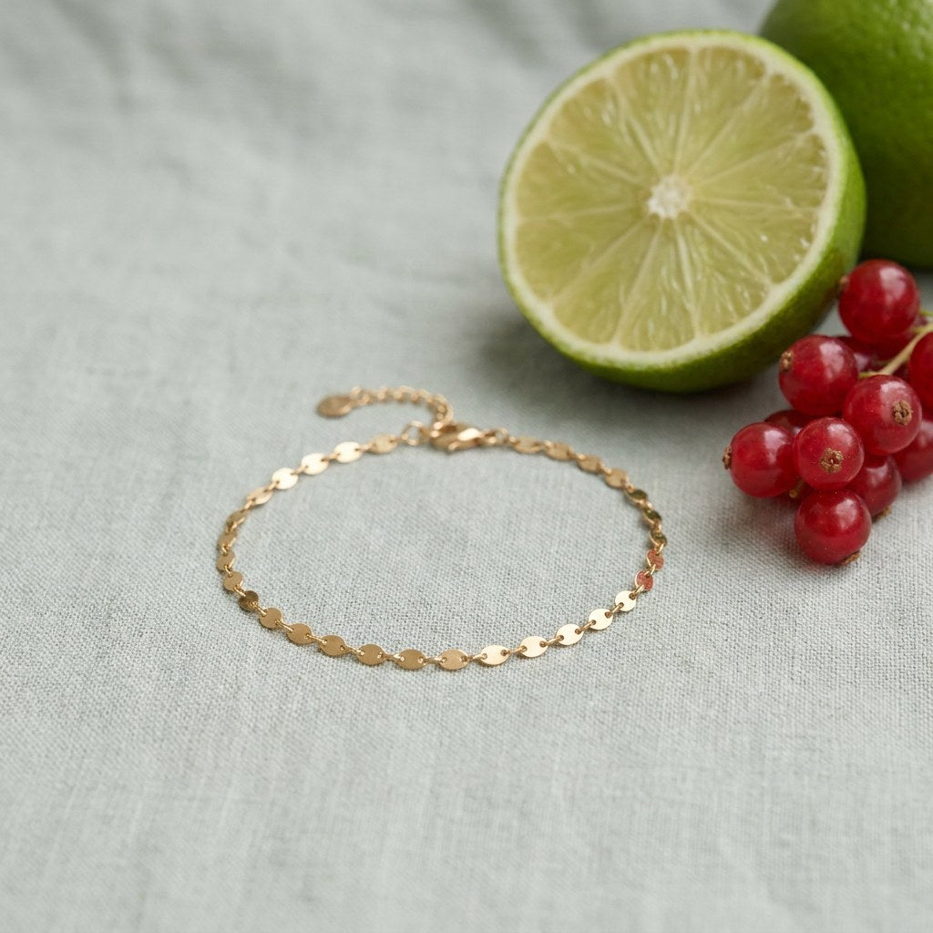 Gold Chain Bracelet on pale grey-green linen beside a halved lime and red currants